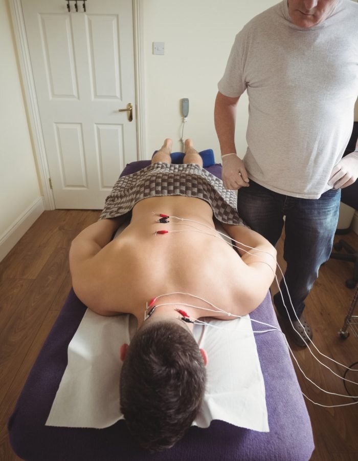 Physiotherapist performing electro dry needling on the back of a patient in clinic